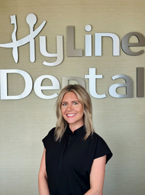A woman standing in front of a sign that reads  Hyloline Dental.