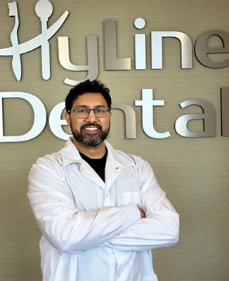 The image shows a man standing in front of a sign for Hyline Dental, wearing a white lab coat.