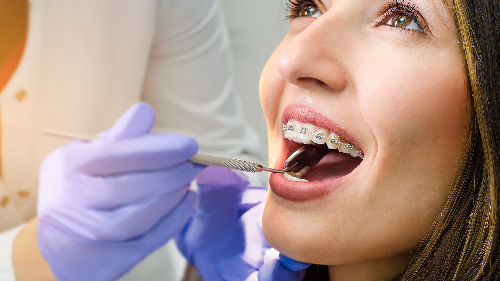 An image of a woman receiving dental care, with a dentist performing an examination and the patient seated in a dental chair.