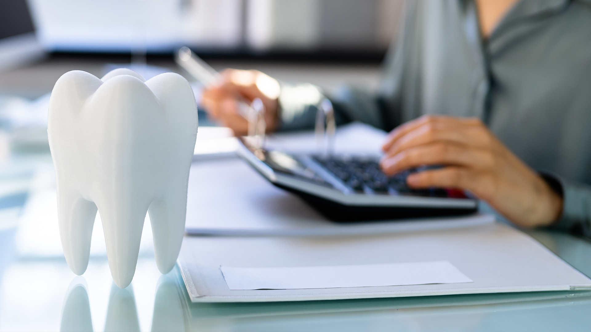 The image shows a person using a computer, with a large 3D tooth model placed on the desk in front of them.