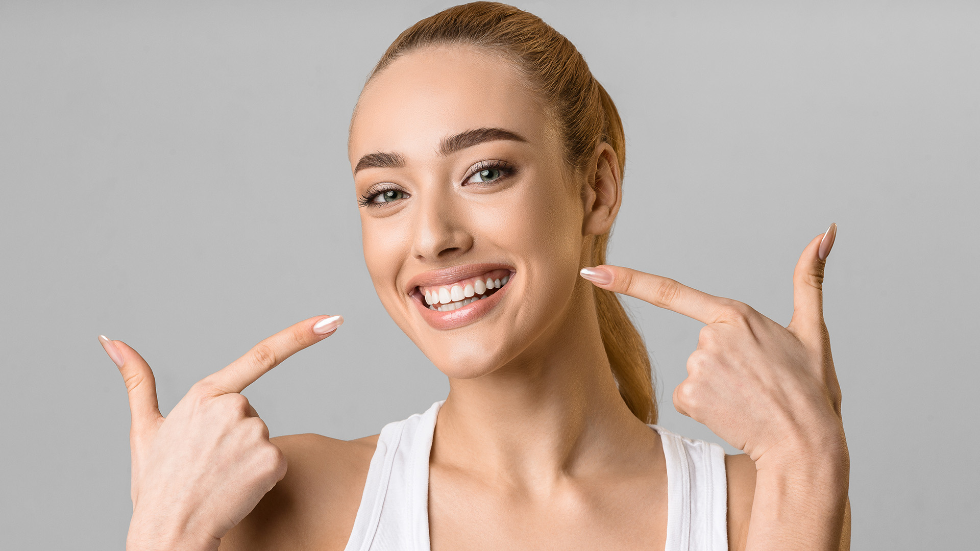 A woman with a bright smile, pointing at her teeth and holding up two fingers, likely indicating the number of teeth or a gesture of approval.