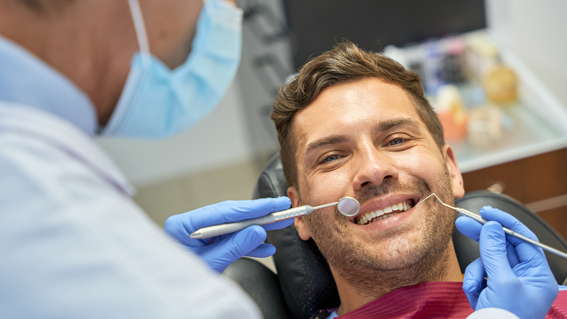 A man in a dental chair receiving treatment, with a smiling expression and a dental hygienist performing the procedure.