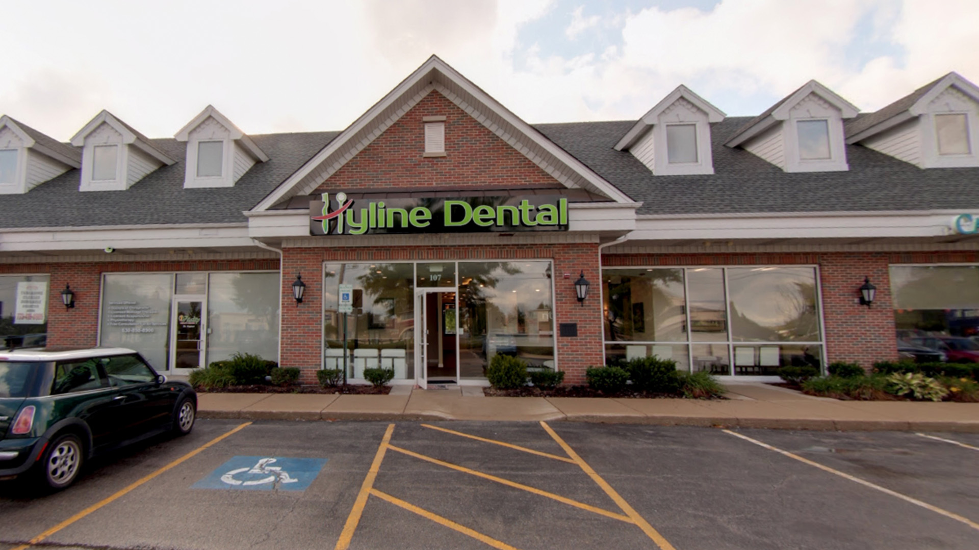 The image shows a dental clinic with a sign that reads  Hygiene Dental  in the foreground, and there is a parking lot with cars visible behind it.