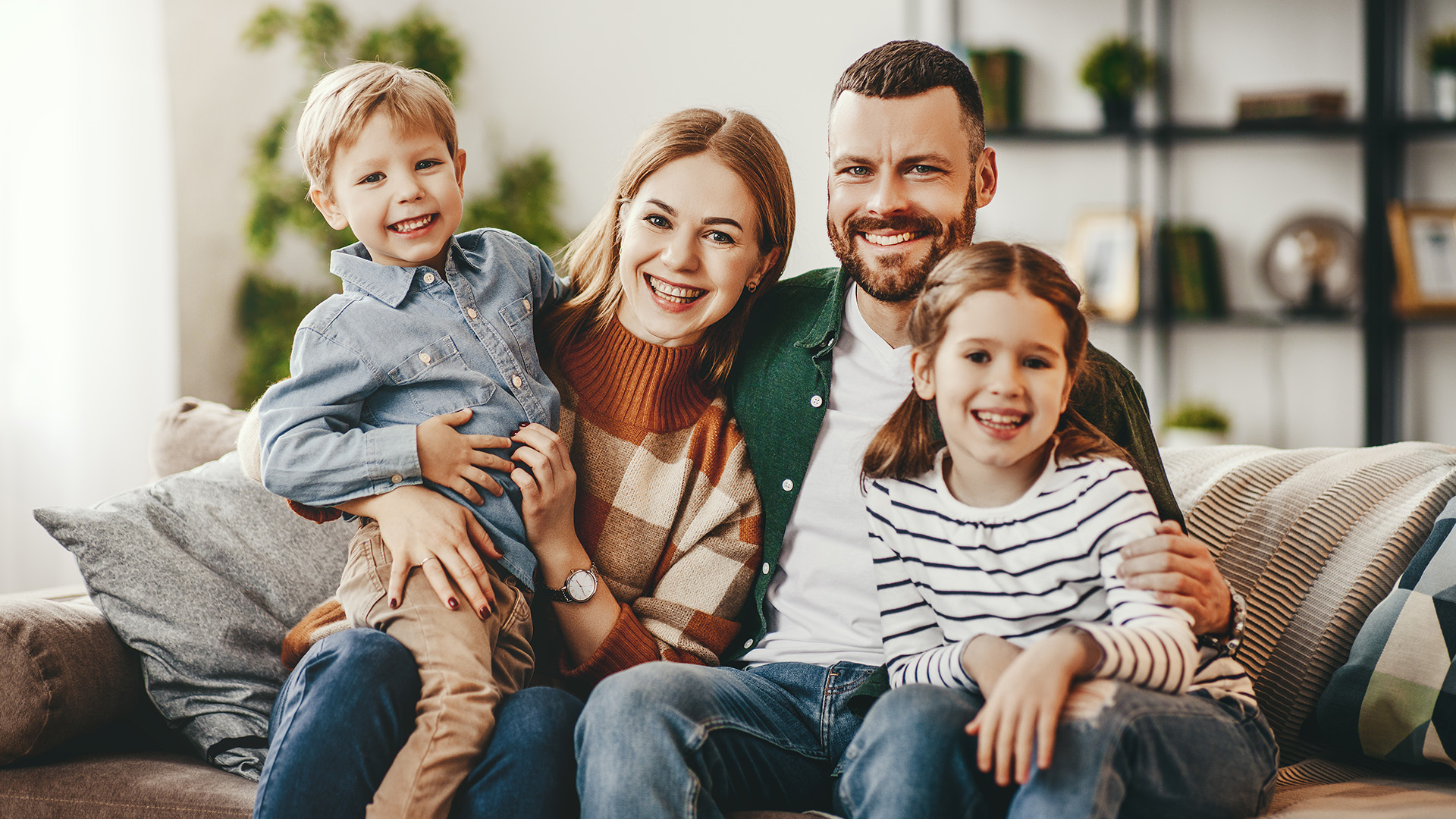 A family of four, including two adults and two children, posing for a photo in a living room setting.