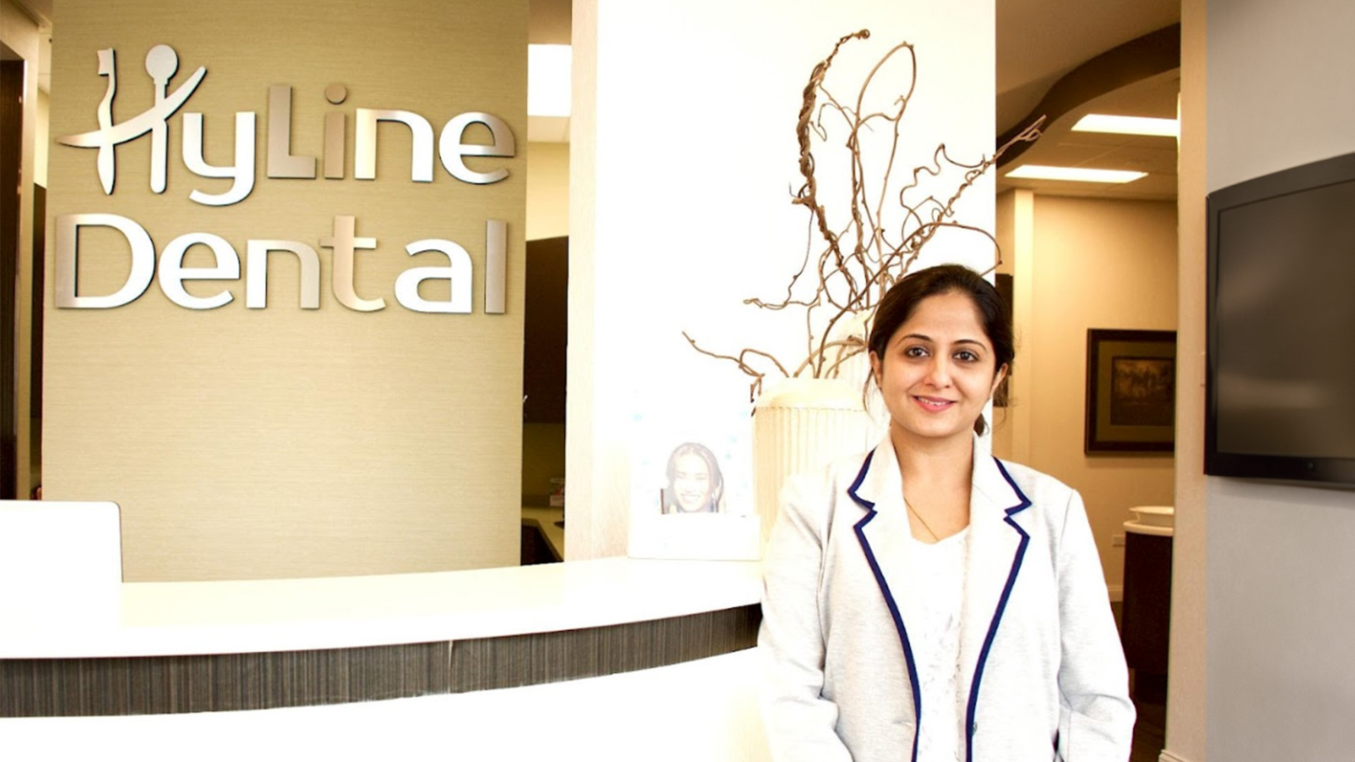 A woman in a professional setting, standing in front of a sign that reads  HYLINE DENTAL .