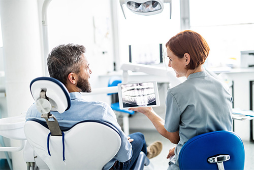 A dental professional showing a patient an image of their teeth on a tablet.
