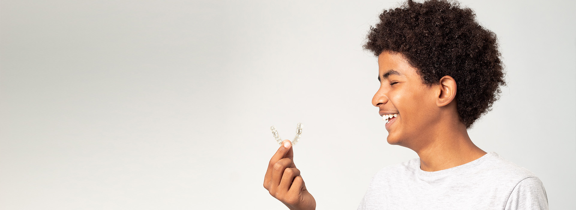 A young person with an open smile, holding a small white flower, against a plain background.