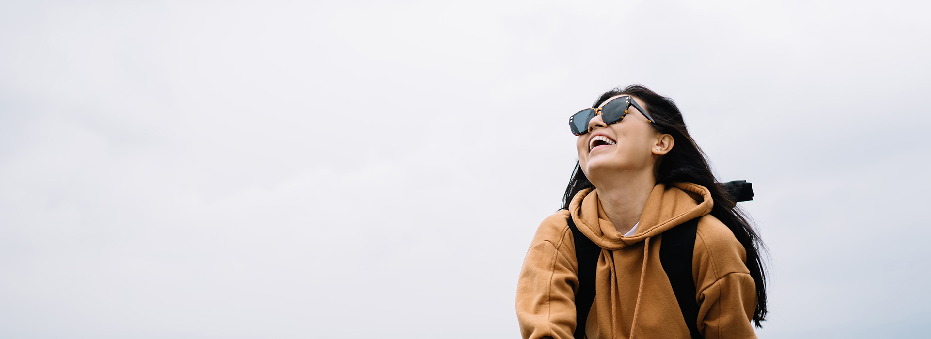 A person in a hoodie stands outdoors, smiling and looking off to the side.