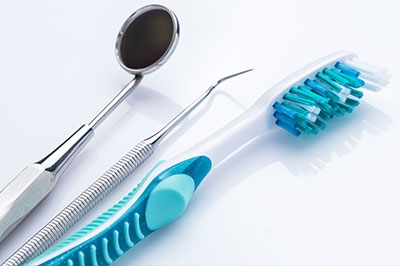 Dental tools including a toothbrush, dental mirror, and tweezers on a white background.