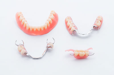 The image displays a set of white dental implants with pink acrylic teeth, arranged in two rows, against a plain background.