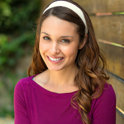 A woman with long hair and a headband, smiling at the camera.