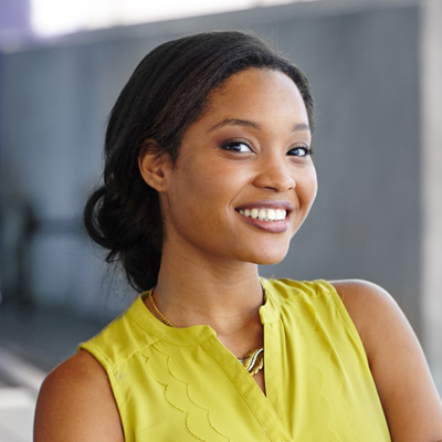 A smiling woman in a yellow top, posing for the photo with a confident expression.