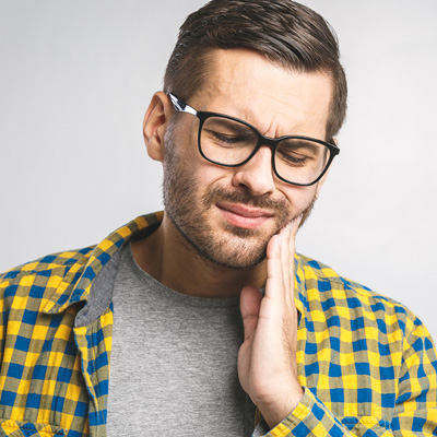 The image depicts a man with glasses and a beard, wearing a plaid shirt, holding his hand to his chin in a thoughtful or contemplative pose. He has a concerned expression on his face as he looks upwards.