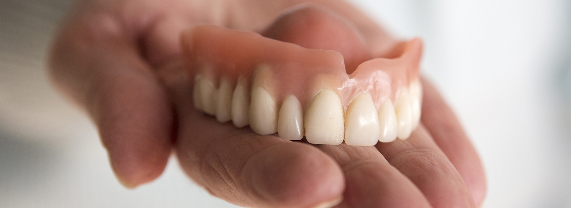 A person s hand holding a set of dentures against a blurred background.