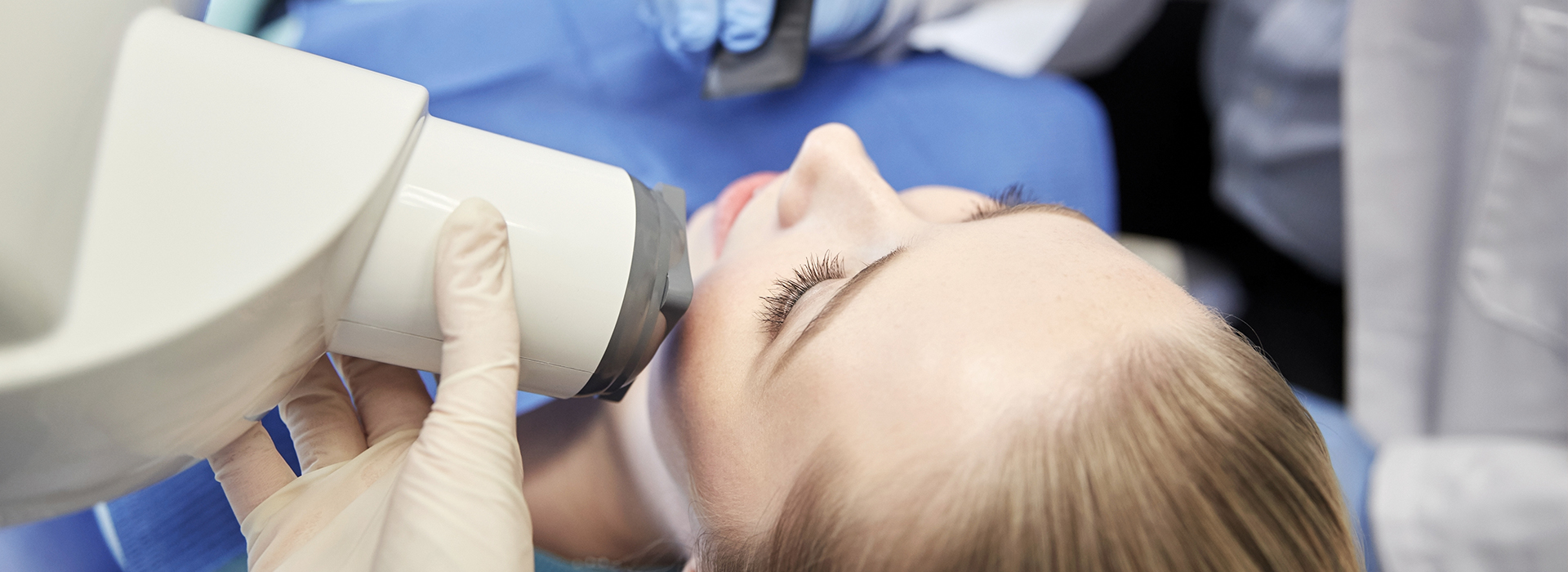 A woman is receiving a dental implant procedure, with a dentist using a microscope to guide the placement of the implant.