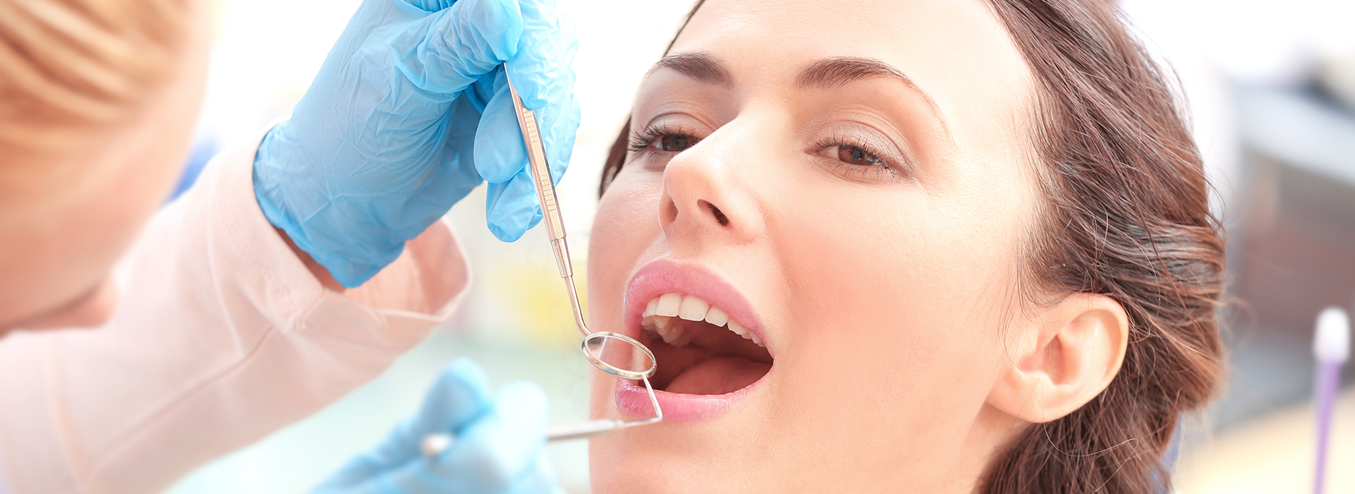 An image of a woman receiving dental treatment, with a focus on the dental hygienist performing the procedure and the dental tools in use.