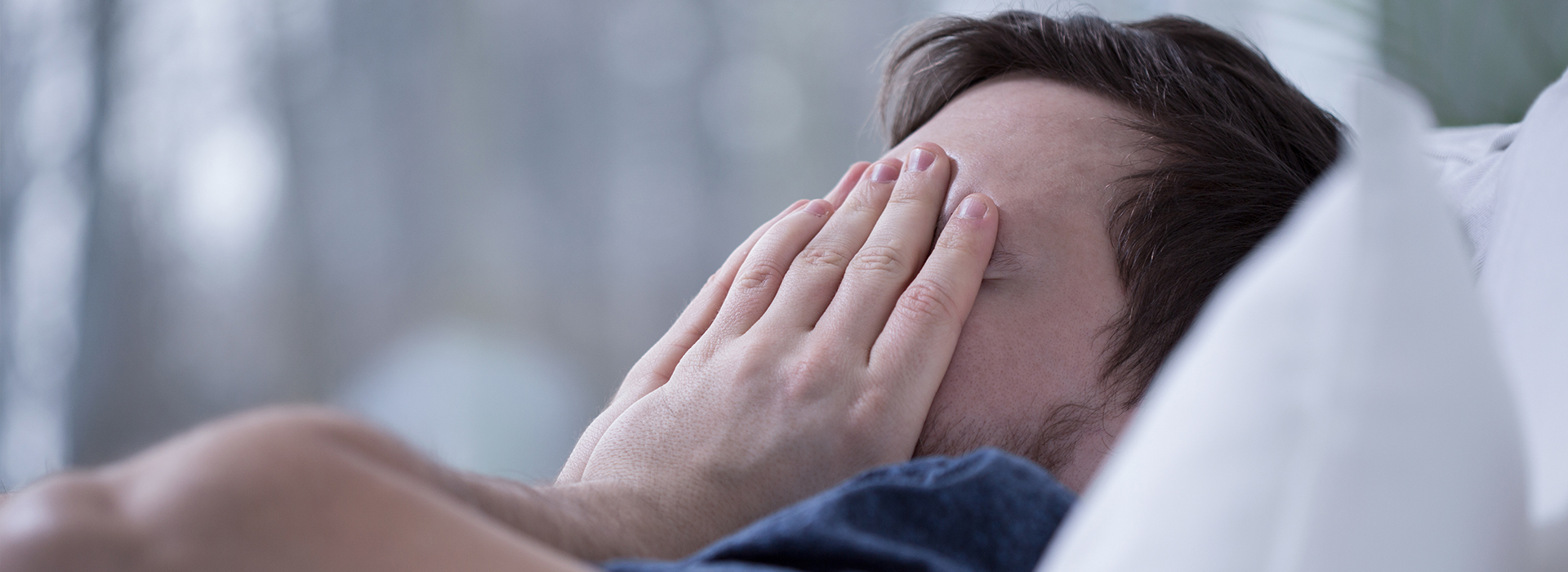 The image shows a person lying in bed with their face partially covered, appearing to be asleep or resting.