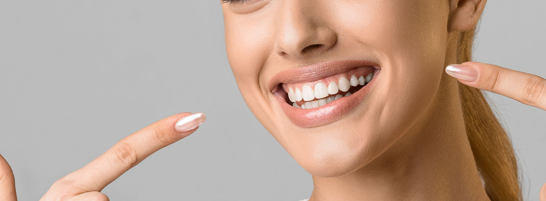 A woman with a radiant smile, showcasing her teeth and holding up a peace sign with both hands.