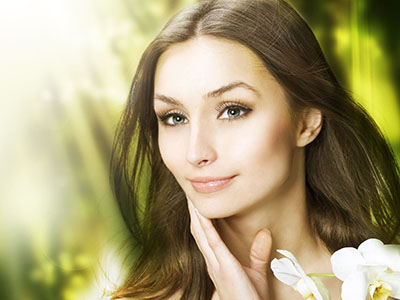 A woman with long hair, wearing makeup and a serene expression, set against a blurred background of greenery.