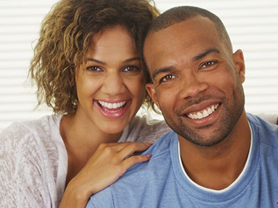 A man and a woman are smiling at the camera, with the man wearing a short beard and both of them looking directly into the lens.