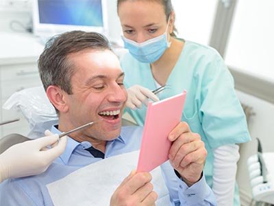 A man sitting in a dental chair, holding up a pink card with a smile, while a dentist and nurse look on.