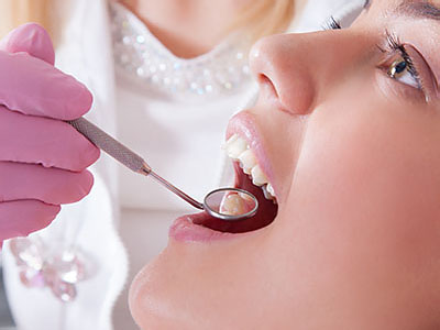 The image shows a dental professional performing a procedure on a patient s teeth, with the patient wearing a pink surgical mask and having their mouth open for treatment.