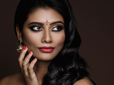 The image features a woman with dark hair, wearing red lipstick and adorned with earrings, posing in front of a neutral background.