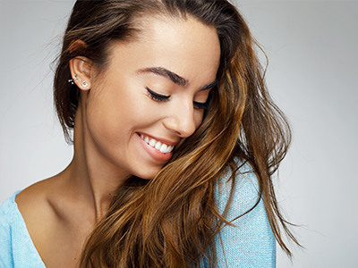 A young woman with long hair, smiling gently while looking down, against a plain background.