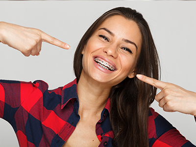 A woman with a big smile, pointing to her teeth, against a white background.