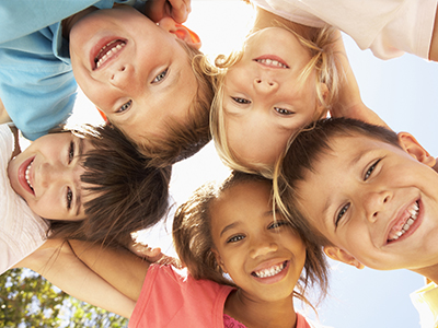 The image depicts a group of children, with varying expressions and poses, gathered in the center against a bright outdoor background.