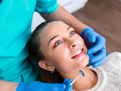 A dental hygienist performing a teeth cleaning procedure on a patient, with the patient s eyes closed and smiling.