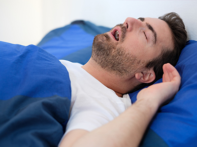 The image shows a man lying in bed with his eyes closed, appearing to be asleep or resting.