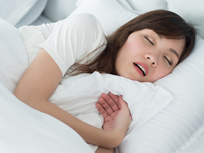 A woman in a white shirt is lying down in bed, with her eyes closed and mouth slightly open as if she s asleep or about to fall asleep.